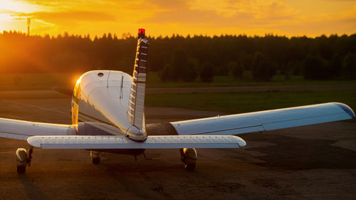 Airplane on airport runway against sky during sunset