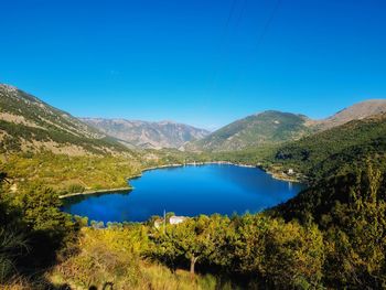 Scenic view of lake and mountains against clear blue sky