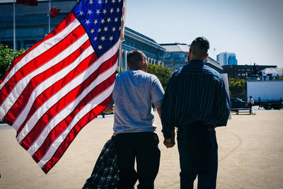 Rear view of gay couple holding hands and walking with american flag