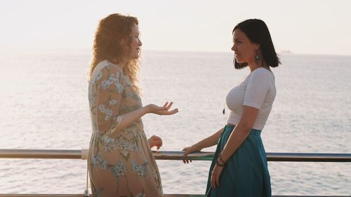 Side view of female friends talking while standing on boat deck against sea