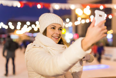 Portrait of smiling woman standing against illuminated light at night