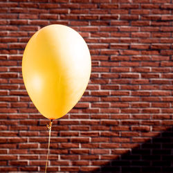 Close-up of yellow balloon against brick wall