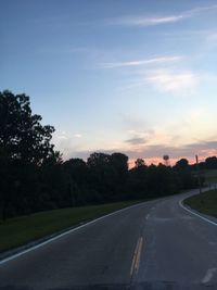 Road by trees against sky during sunset