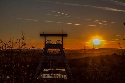 Silhouette built structure on field against sky during sunset