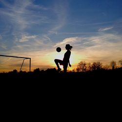 Silhouette woman playing soccer on field at sunset
