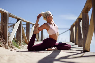 Young woman exercising on footbridge against sky