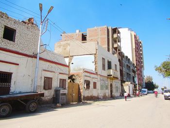 Buildings by road against blue sky