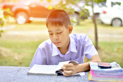 Boy reading book while sitting in park