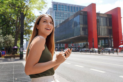 Woman hail a vehicle using mobile app waiting for taxi or uber on paulista avenue, sao paulo, brazil