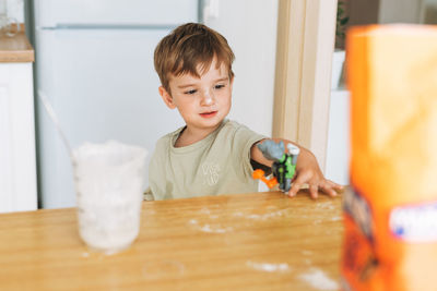 Toddler boy have fun while cooking with flour at the table in kitchen at home. boy playing with toy