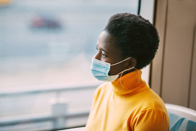 Young african woman wearing a protective mask rides on a bus and looks out the window. coronavirus
