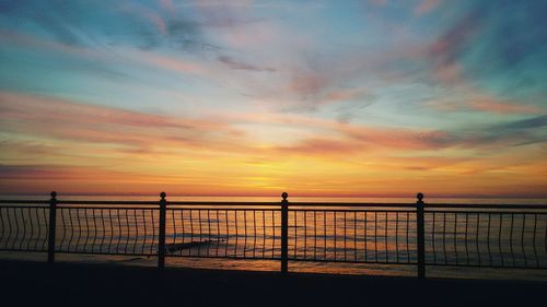 Silhouette railing by sea against sky during sunset