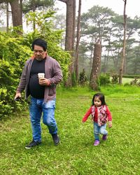 Father and daughter walking on field against trees