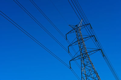 Low angle view of electricity pylon against clear blue sky