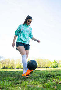 Full length of woman practicing with soccer ball against sky