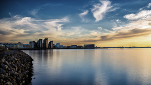 Buildings by sea against sky during sunset