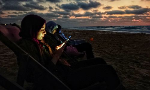 People sitting on beach against sea during sunset
