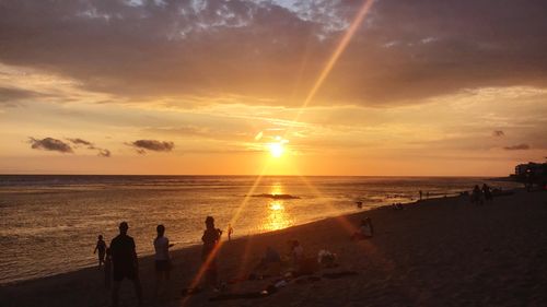 Silhouette people on beach against sky during sunset