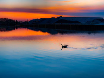 Silhouette man by lake against orange sky