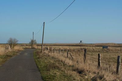 Road amidst field against clear blue sky