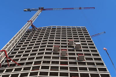 Low angle view of crane by building against clear blue sky