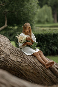 Portrait of young woman sitting on tree trunk