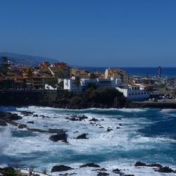 Buildings by sea against clear blue sky