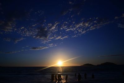 Silhouette people at beach against sky during sunset