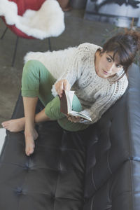 High angle view of woman with book relaxing on sofa at home