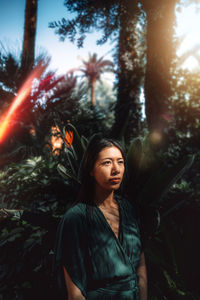 Young woman looking away while standing against trees