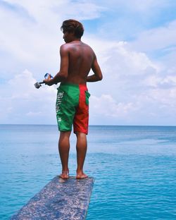 Rear view of shirtless man standing on diving platform