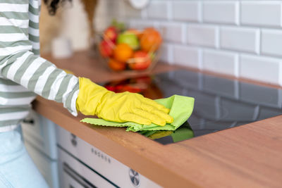 Horizontal of faceless cropped female washing induction hob in yellow gloves with green washcloth