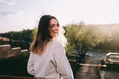 Portrait of beautiful young woman looking away against car