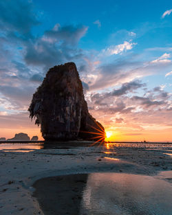 Rock formation on beach against sky during sunset