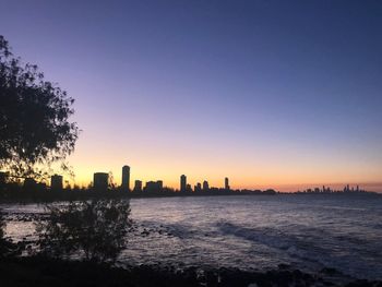 Silhouette buildings in city against clear sky during sunset