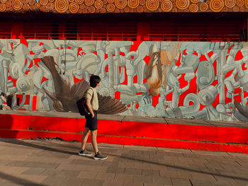Full length rear view of man standing against graffiti wall