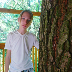 Portrait of teenage girl standing by tree trunk in forest
