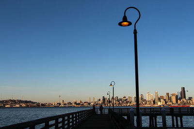 Illuminated street light by city against clear blue sky