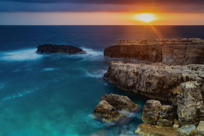 Rocks in sea against sky during sunset