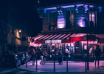 People on street against illuminated buildings in city at night