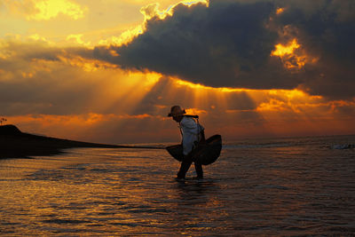 Man with baskets wading in sea against sky