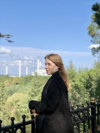 Side view of young woman standing by railing against sky