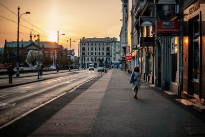 Rear view of woman walking on sidewalk in city during sunset