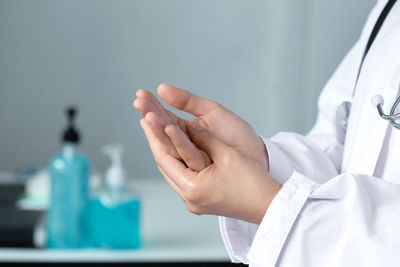 Midsection of doctor applying sanitizer on hands in office