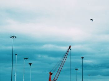 Low angle view of crane and floodlight against sky