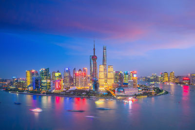 Illuminated buildings by river against sky at night