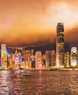 Illuminated buildings by river against sky in city