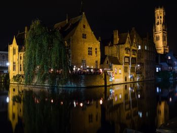 Illuminated buildings by lake in city at night