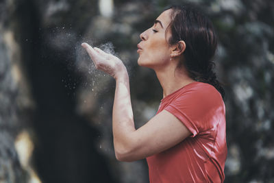 Side view of young woman blowing sports chalk while standing outdoors