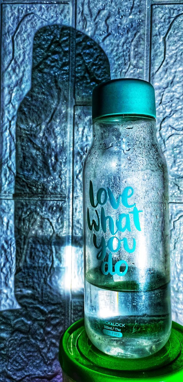 CLOSE-UP OF GLASS BOTTLE AGAINST BLUE BACKGROUND